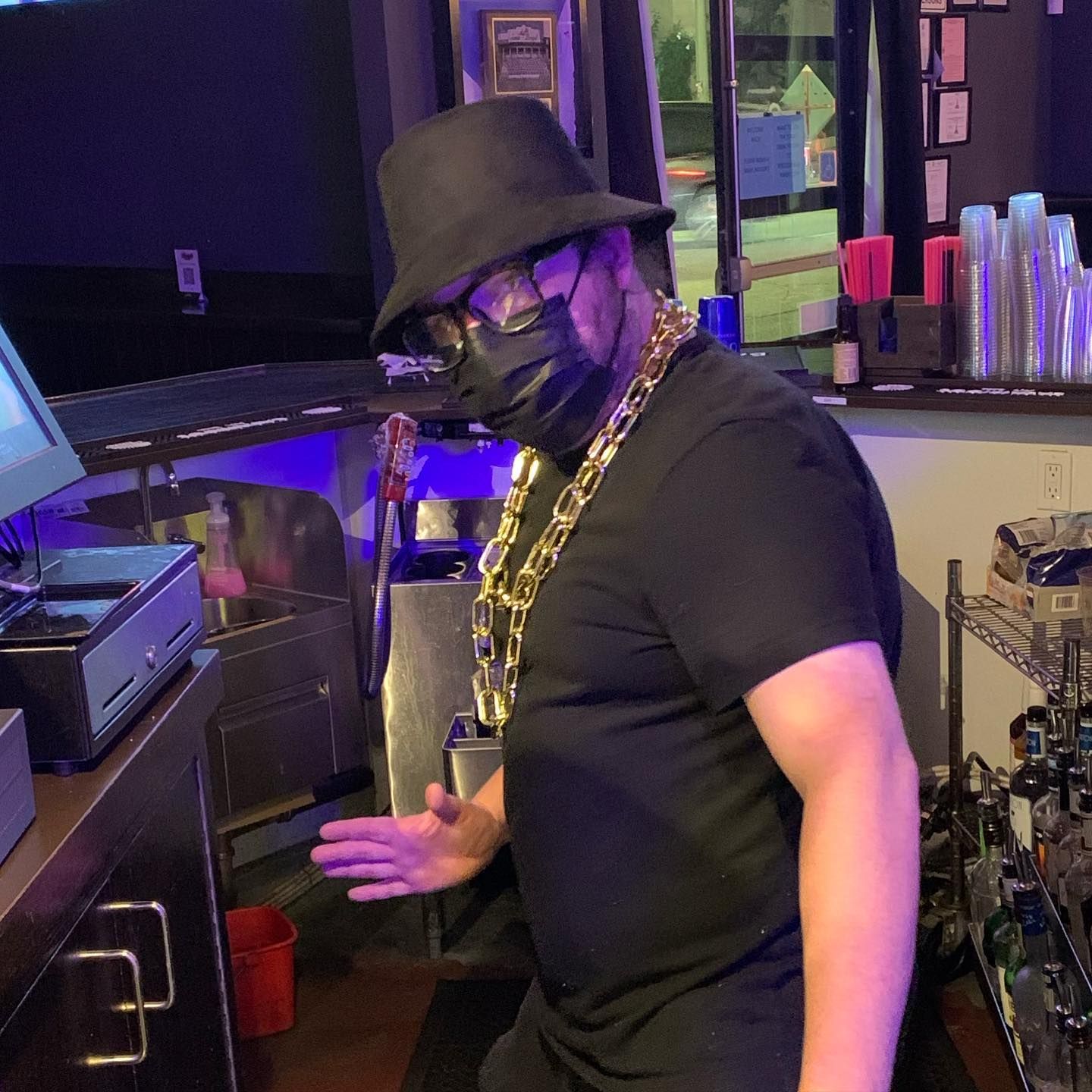 A man wearing a mask and a hat is standing in front of a counter