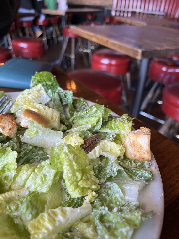 A close up of a plate of caesar salad on a table in a restaurant.
