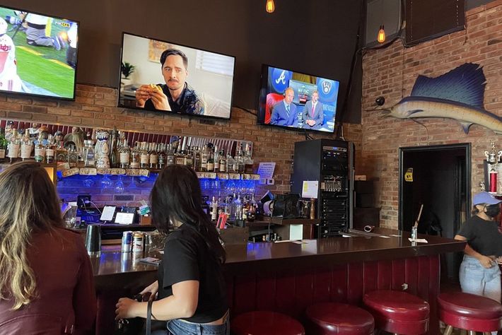 A group of people are sitting at a bar watching television.