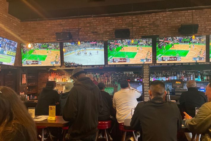 A group of people are sitting at a bar watching sports on television.