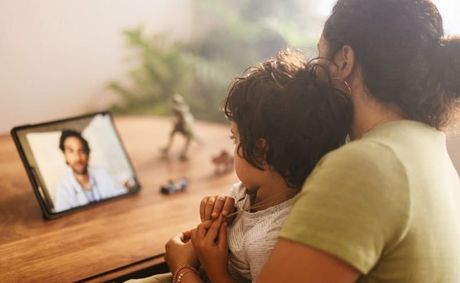 A woman is holding a child while having a video call with a doctor.