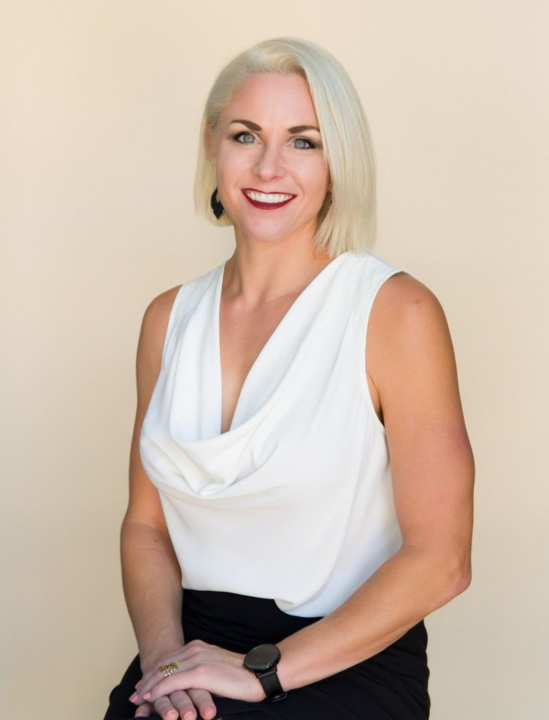 A woman in a white top and black skirt is sitting on a stool.