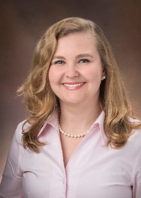 A woman in a pink shirt and pearl necklace is smiling for the camera.