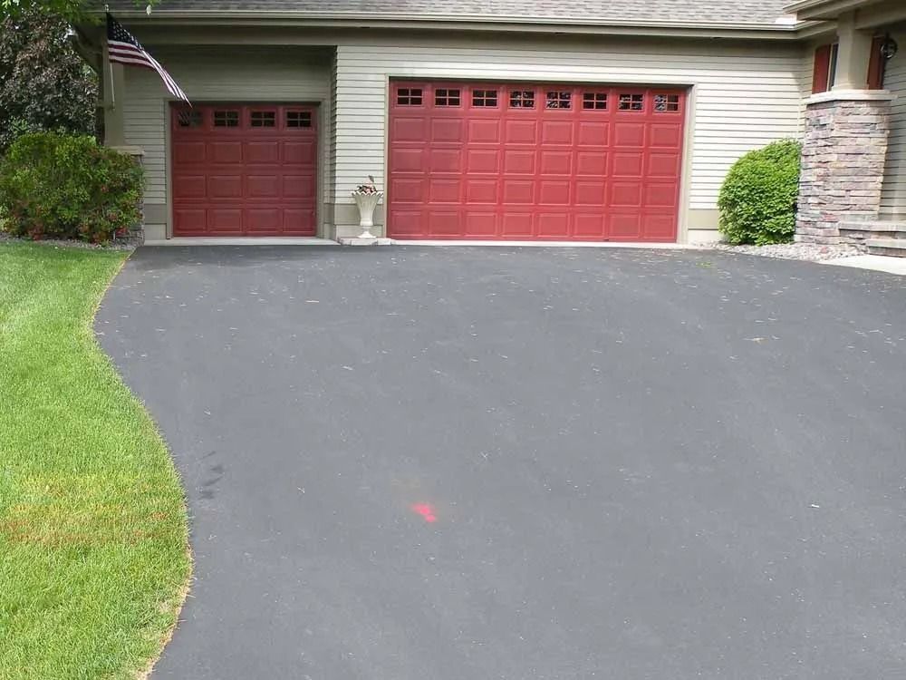 A residential house exterior with two red garage doors, a paved driveway, and a small patch of grass.