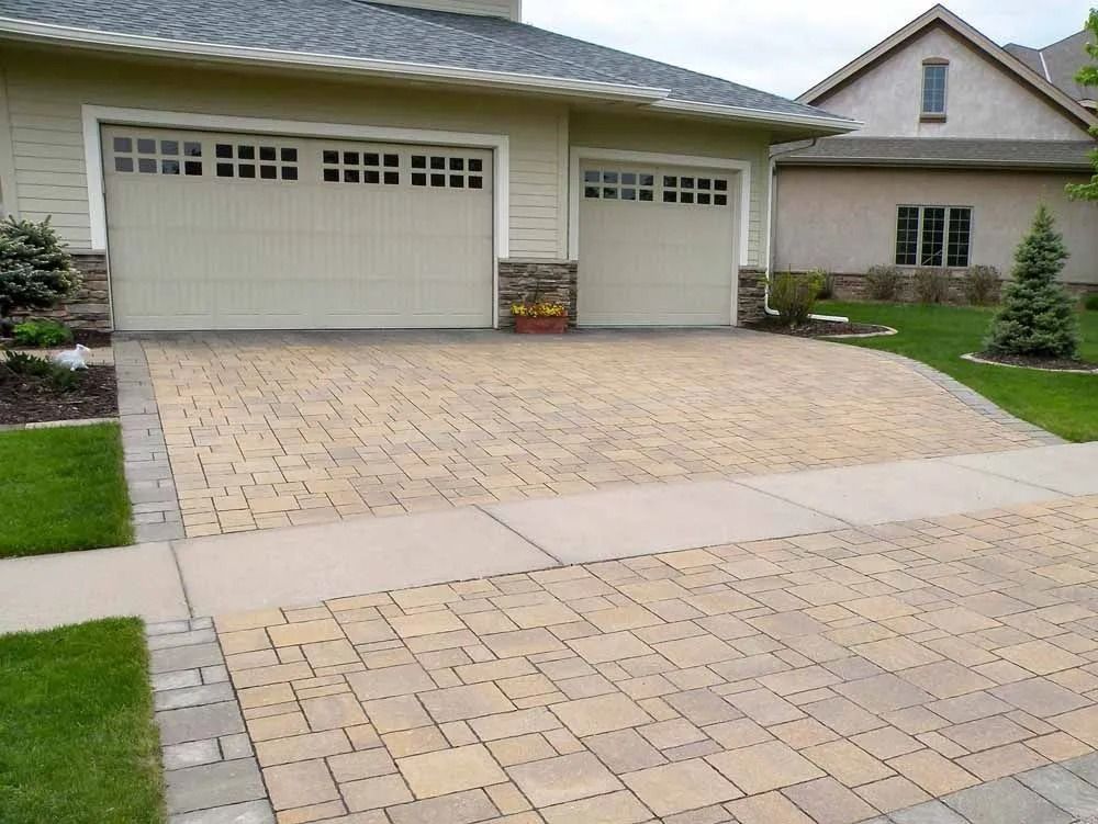 A suburban house with a two-car garage and a paved stone driveway in front of a sidewalk and grass lawn.