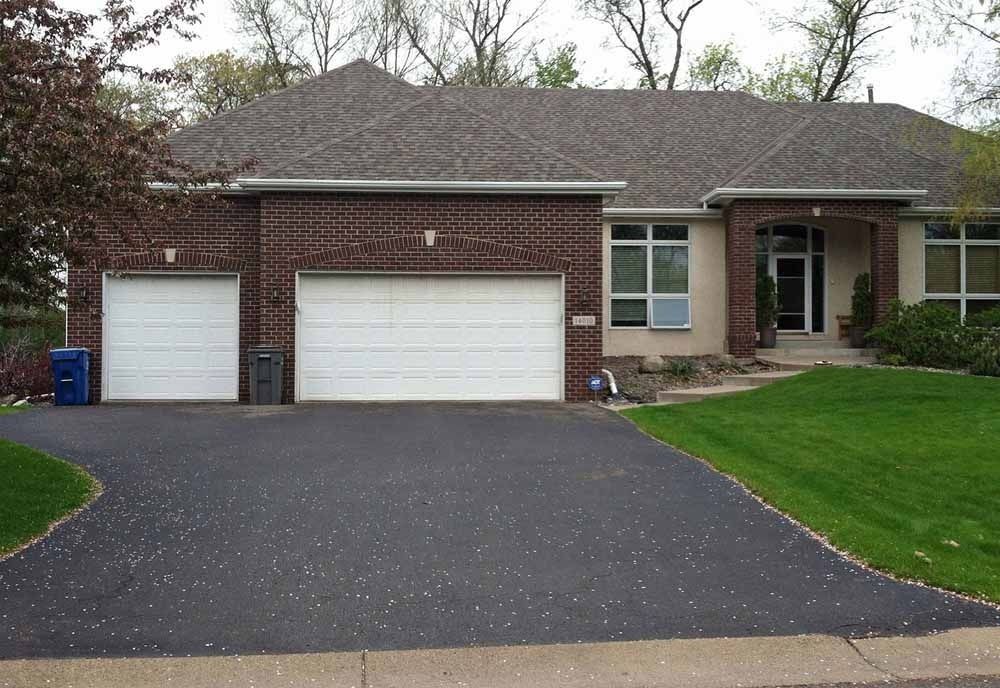 A single-story brick house with a multi-car garage and asphalt driveway under a gray roof on a clear day.