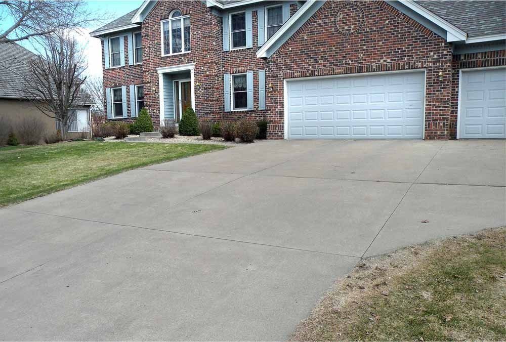 A two-story brick house with a concrete driveway and two white garage doors, viewed from the street.