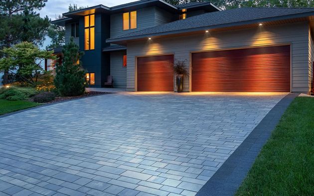 A modern, two-story house with a three-car garage and a stone paver driveway at dusk.