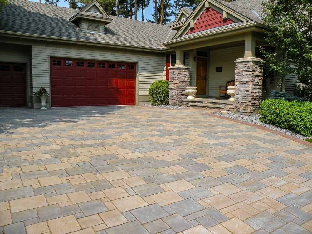 A paved driveway made of multi-colored rectangular stone blocks in front of a house with a red garage door.