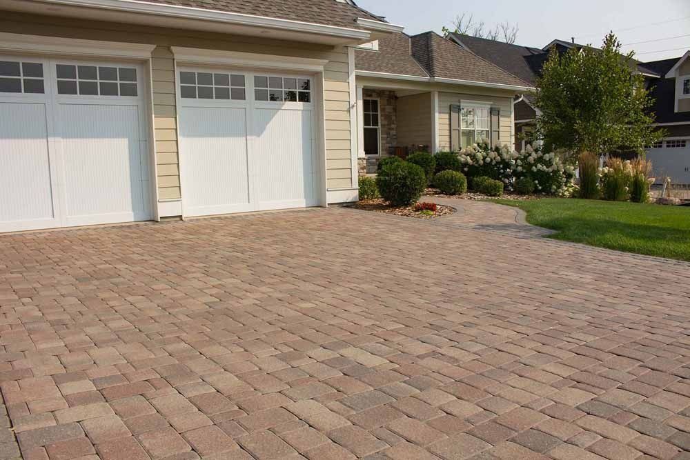 A paved driveway made of multi-toned brick pavers leading up to a two-car garage and home entrance.