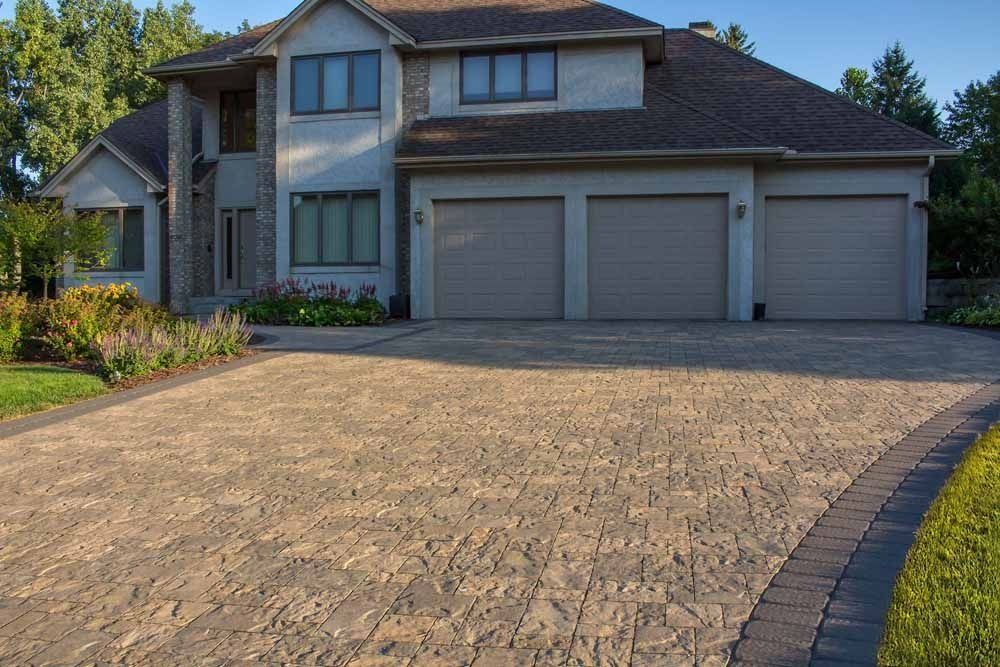 A large, light-colored house with a three-car garage and a stone-paved driveway.