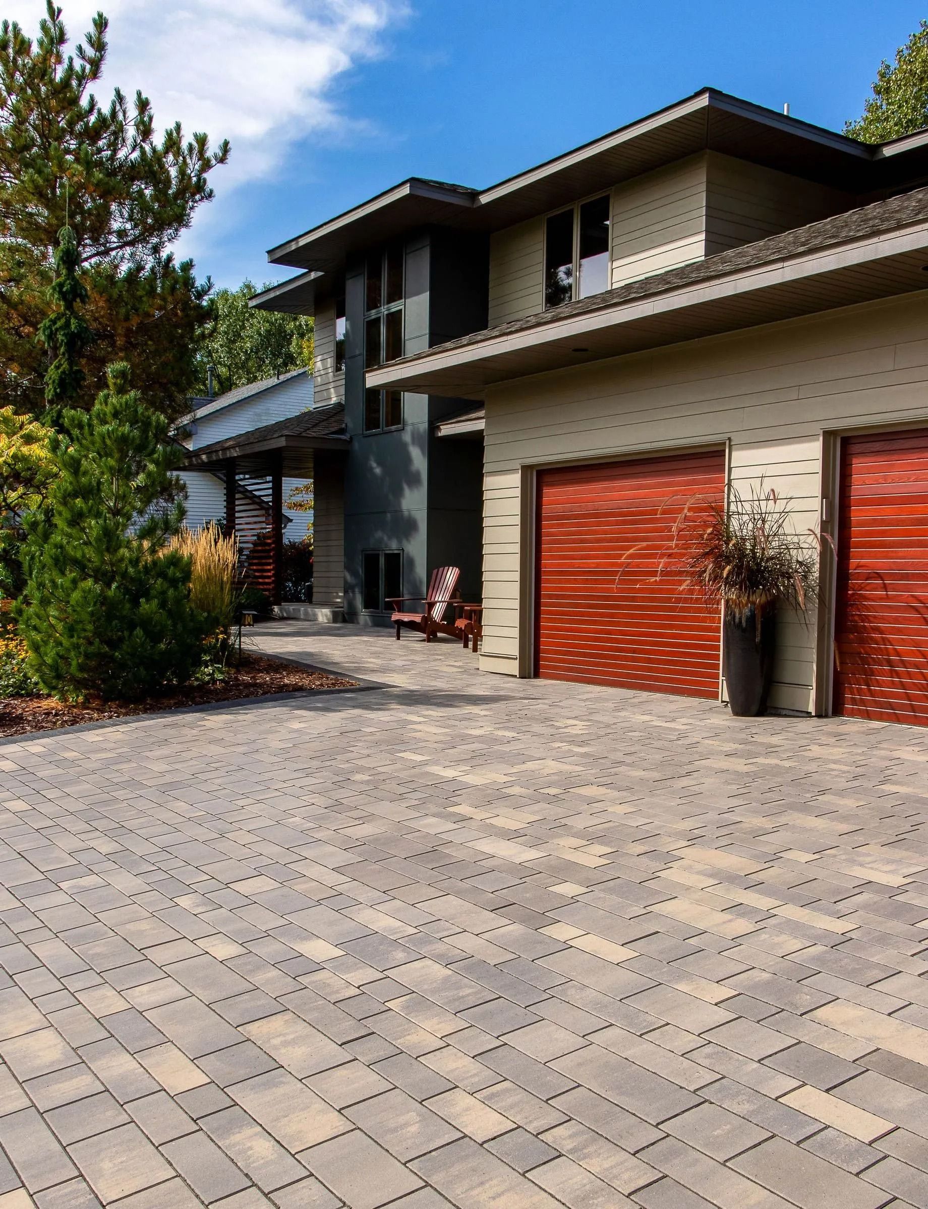 Modern two-story house with a paved driveway, tan stone siding, and two prominent reddish-brown wooden garage doors.