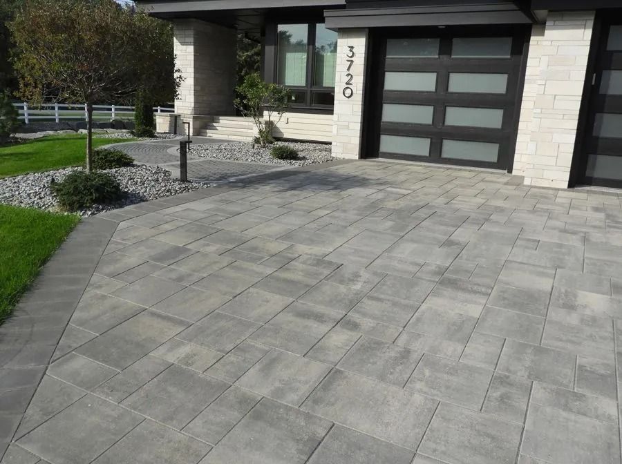 Modern home exterior with a multi-toned gray stone paver driveway and a landscaped gravel front yard.