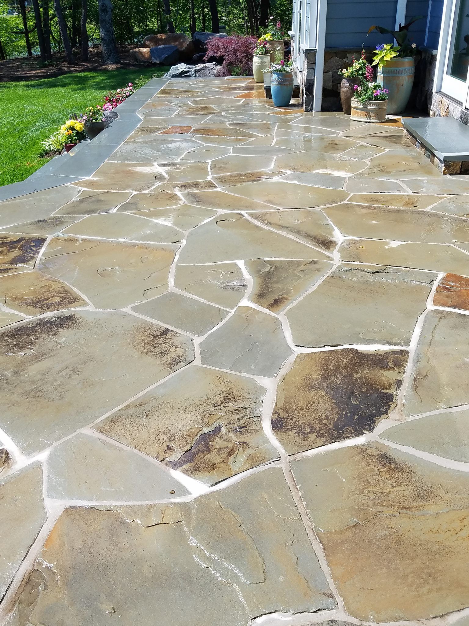 Stone patio with irregular flagstones beside a house, wet from water or cleaning.