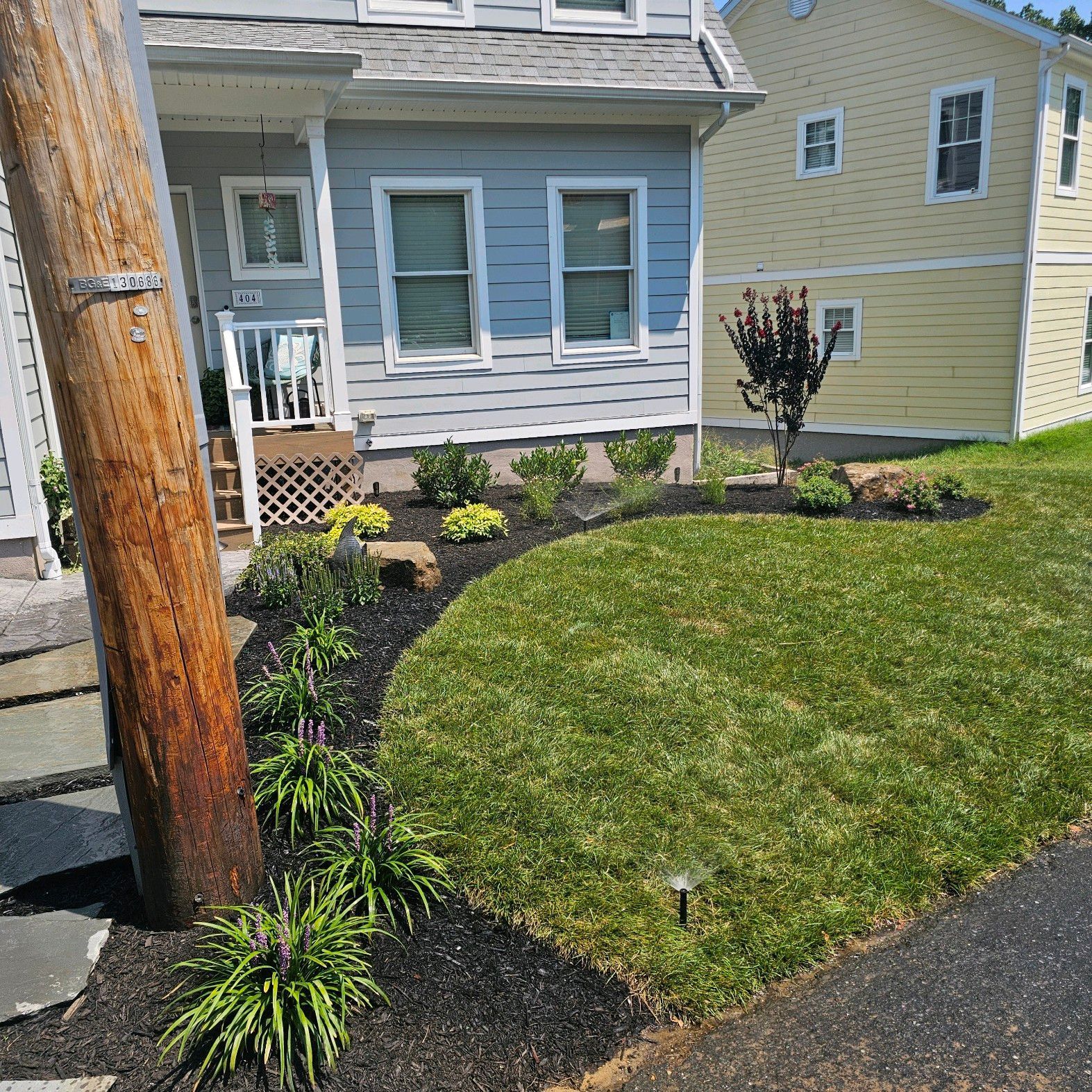 Front yard with green lawn, mulch beds, and a gray house beside a wooden utility pole