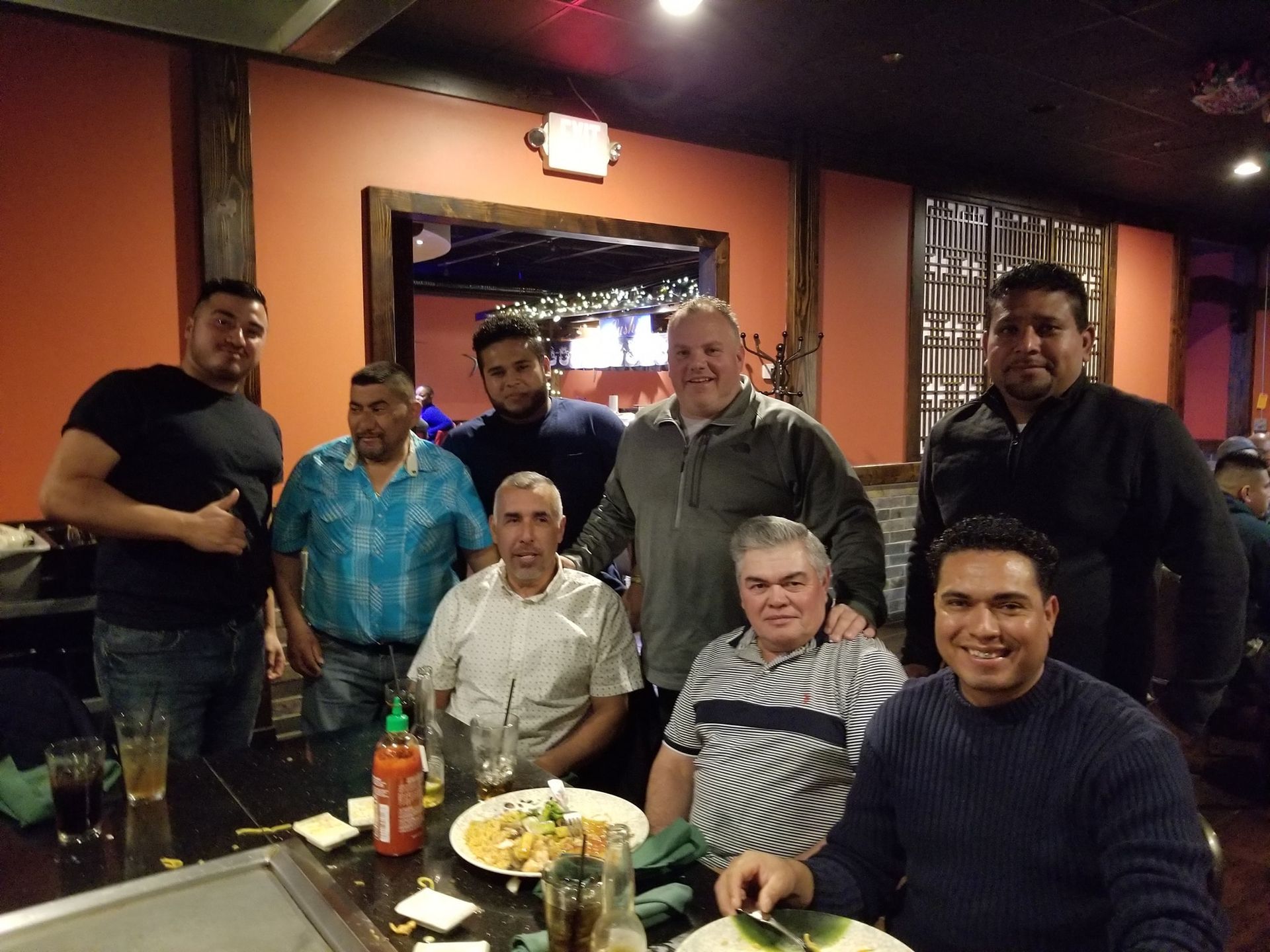 Group of people posing together at a restaurant table, smiling under warm indoor lighting.
