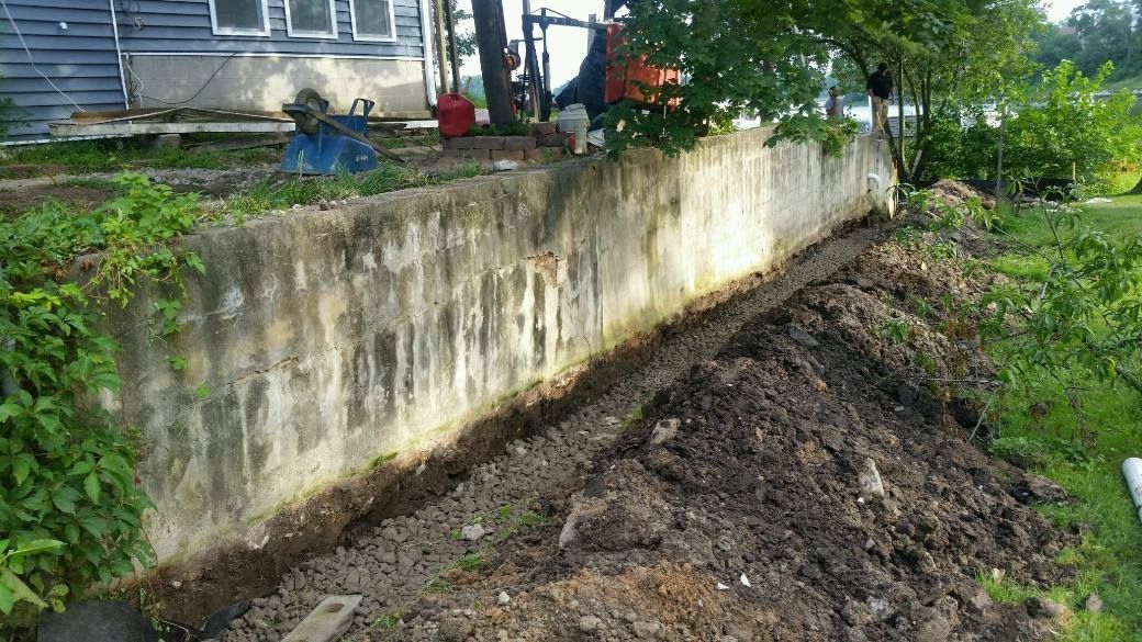 Dirt piled along a stained concrete retaining wall beside a house and green yard.