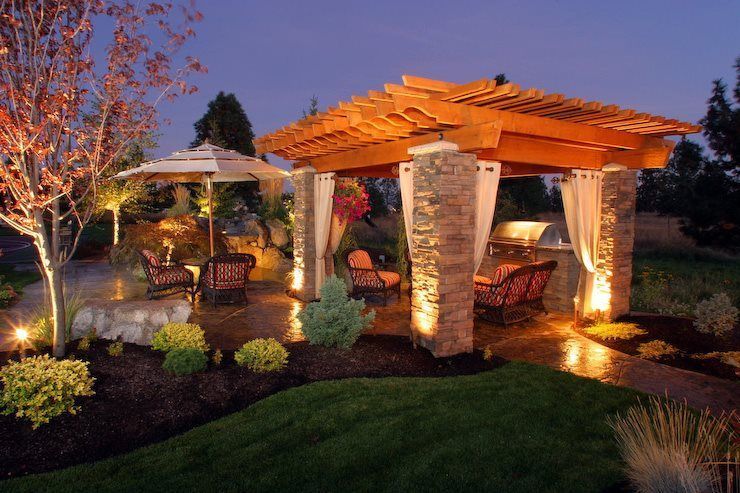 Lit pergola and gazebo in a landscaped garden at dusk with warm lighting and stone pillars