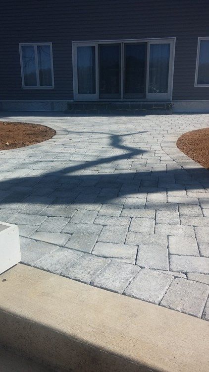 Stone-paved courtyard with a dark building and glass doors, crossed by a long tree shadow