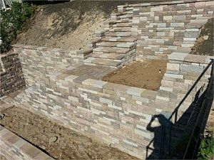 Stone retaining wall with steps built into a sloped dirt hillside, viewed from below