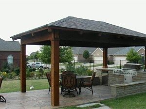Wooden gazebo with table and chairs in a landscaped park patio area.