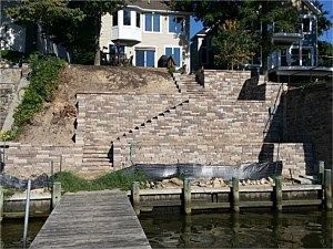 Stone stairs lead from a dock to a blue-and-white house on a waterfront hillside.