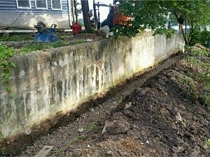 Concrete retaining wall beside a muddy dirt slope and house yard after erosion