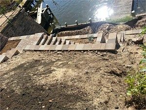 Damaged stone walkway over a steep dirt slope beside a glinting body of water