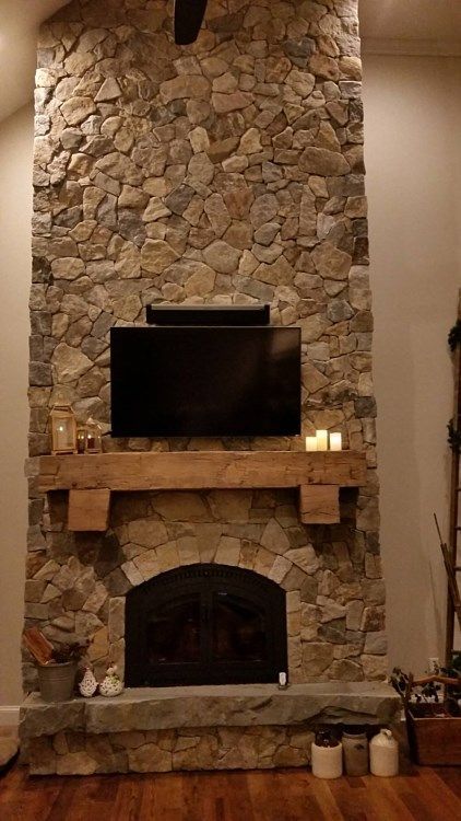 Rustic stone fireplace with a mounted TV, wood mantel, and candles in a cozy living room