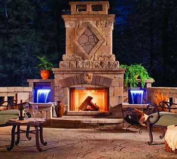 Stone patio with a lit fireplace, blue water features, and outdoor seating at night