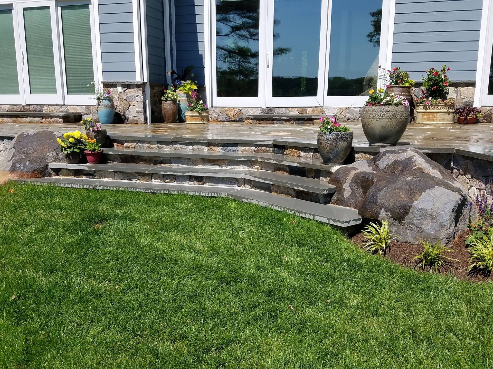 Stone steps and flower pots in front of a house with a bright green lawn