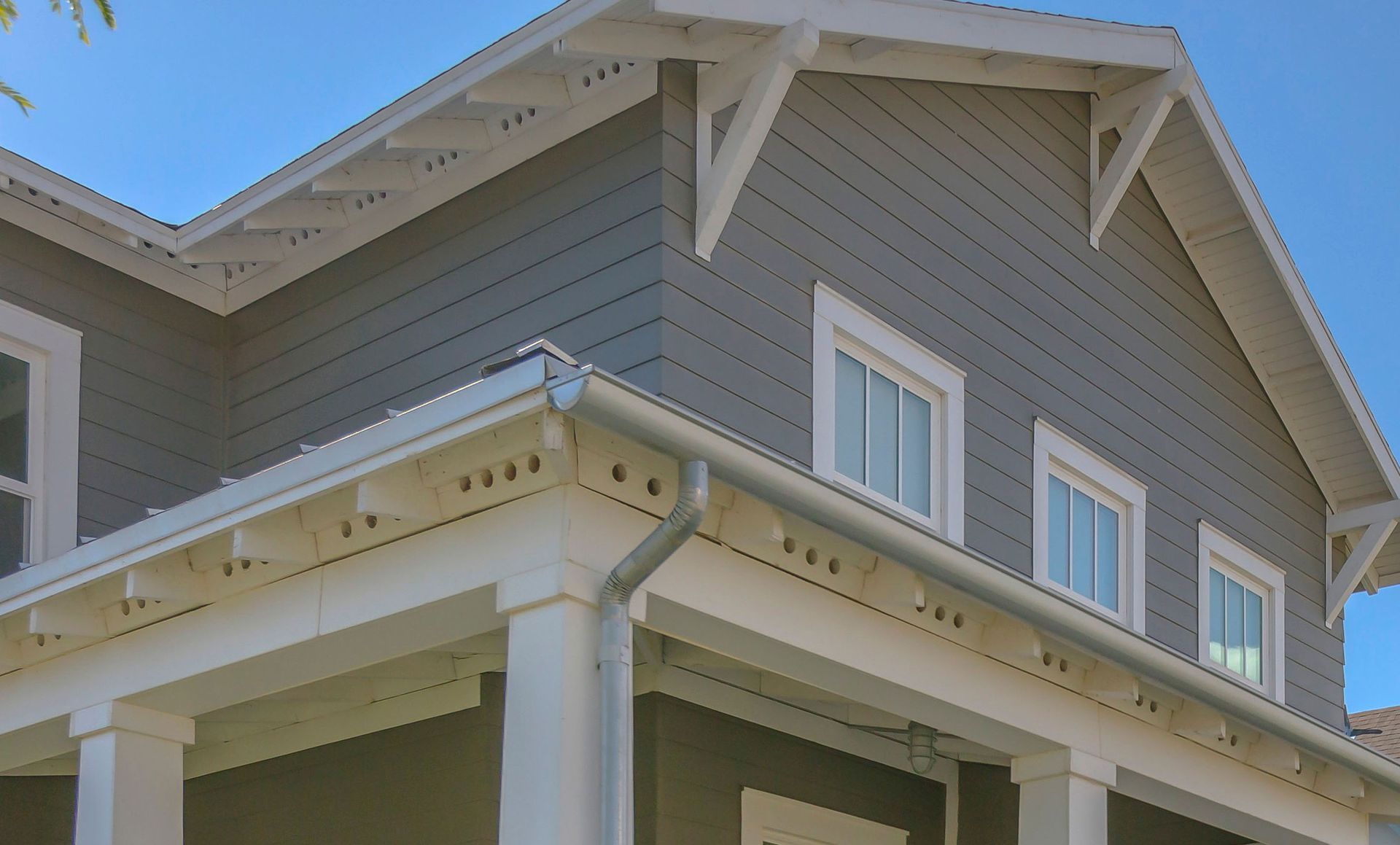 Close-up of a gray house roof with white trim and decorative eaves against a blue sky