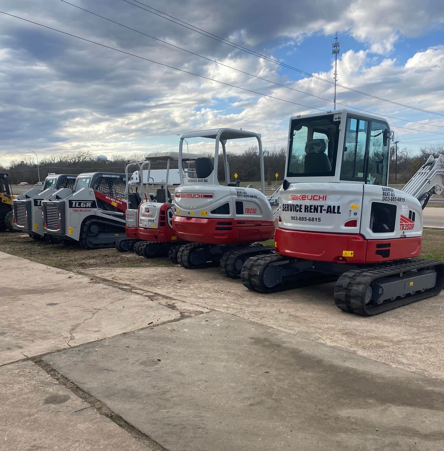Row of red and white construction vehicles with black tracks parked on concrete.