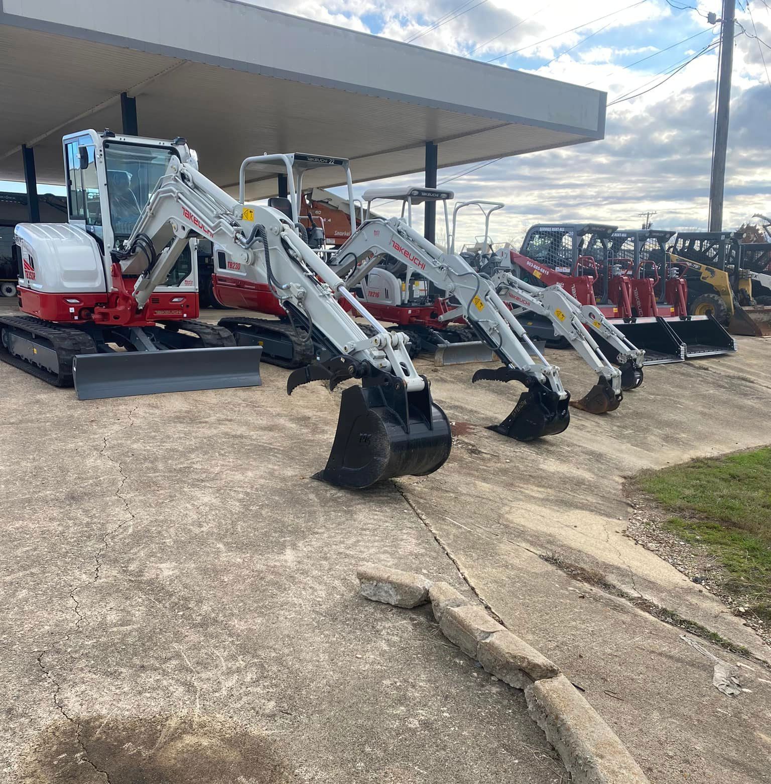 Several white and red track excavators parked outside under a covered area.