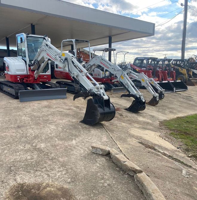 Several white and red track excavators parked outside under a covered area.