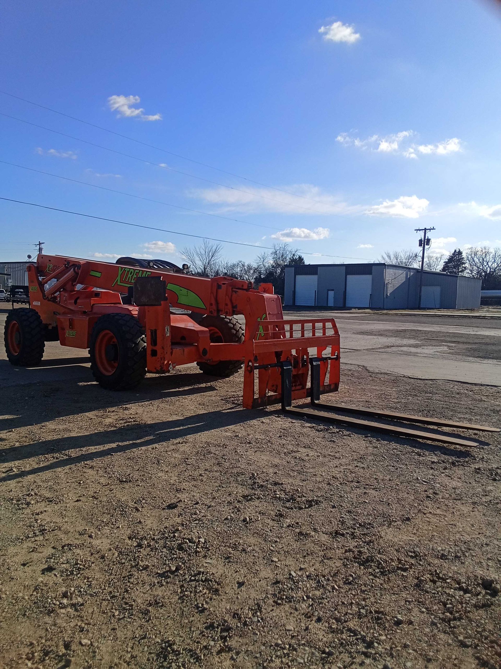 Orange telescopic forklift in a gravel lot under a blue sky.