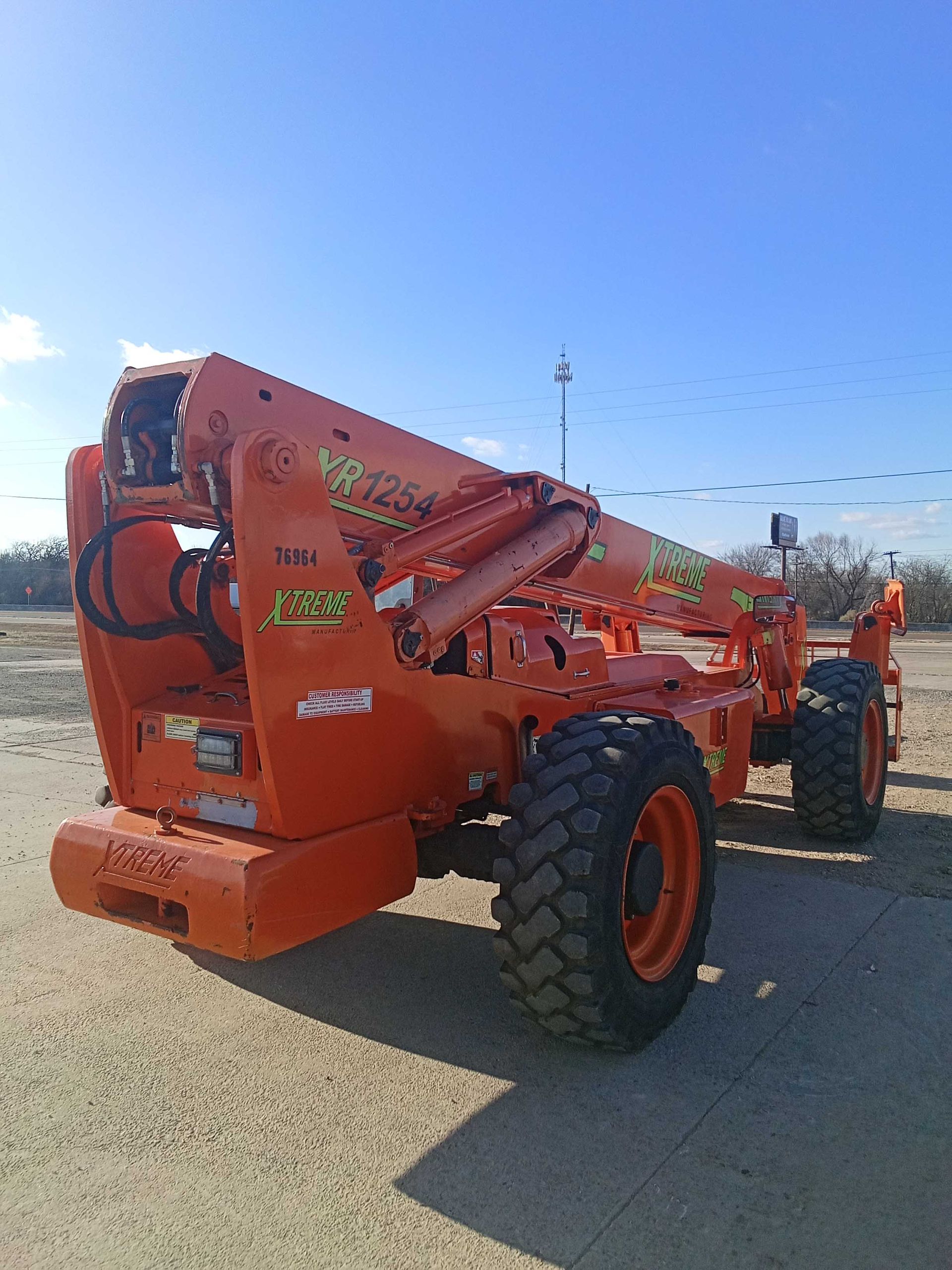 Orange telescopic handler on a dirt surface under a blue sky.