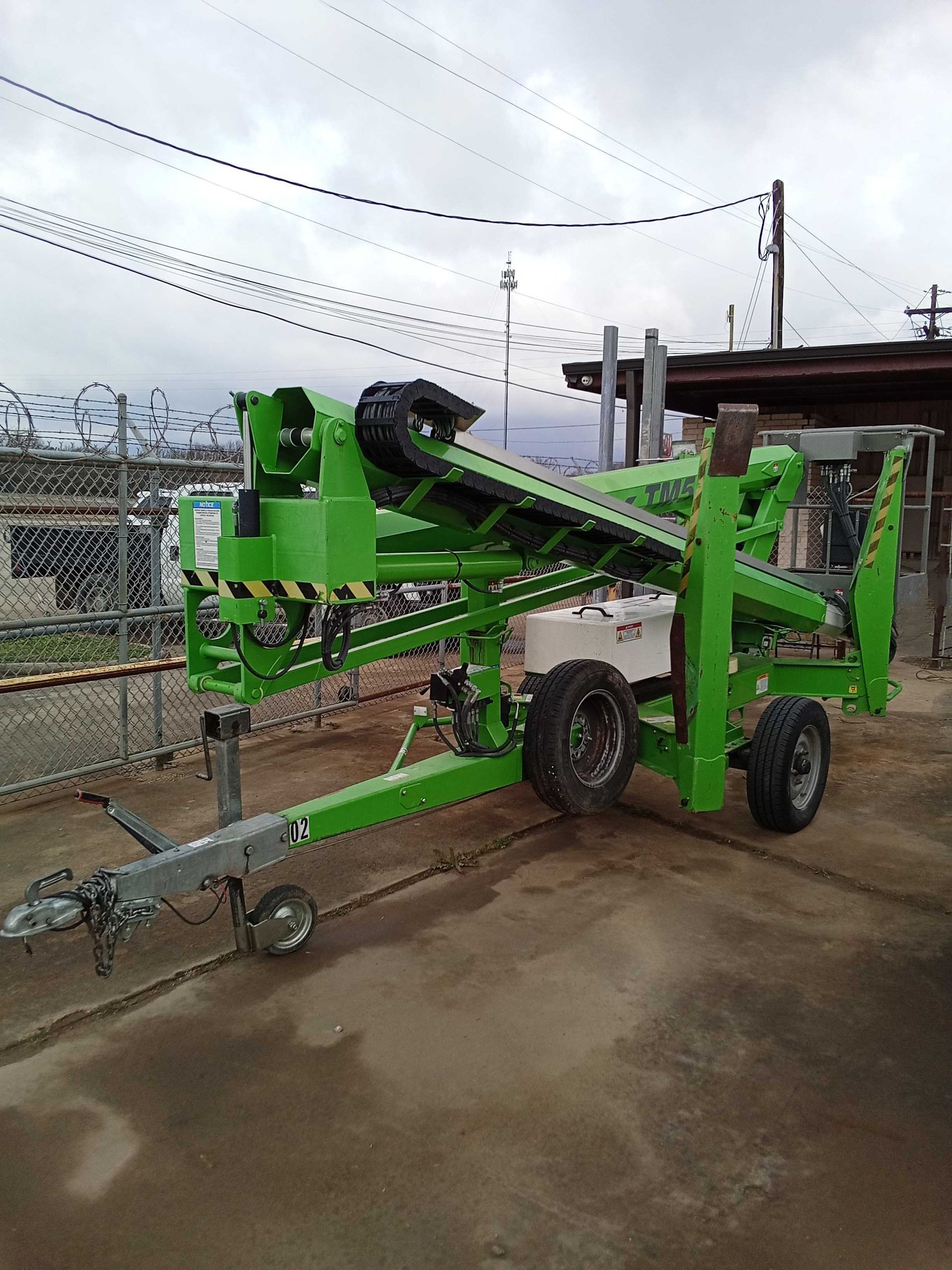 Green towable tree-pruning lift parked outside.