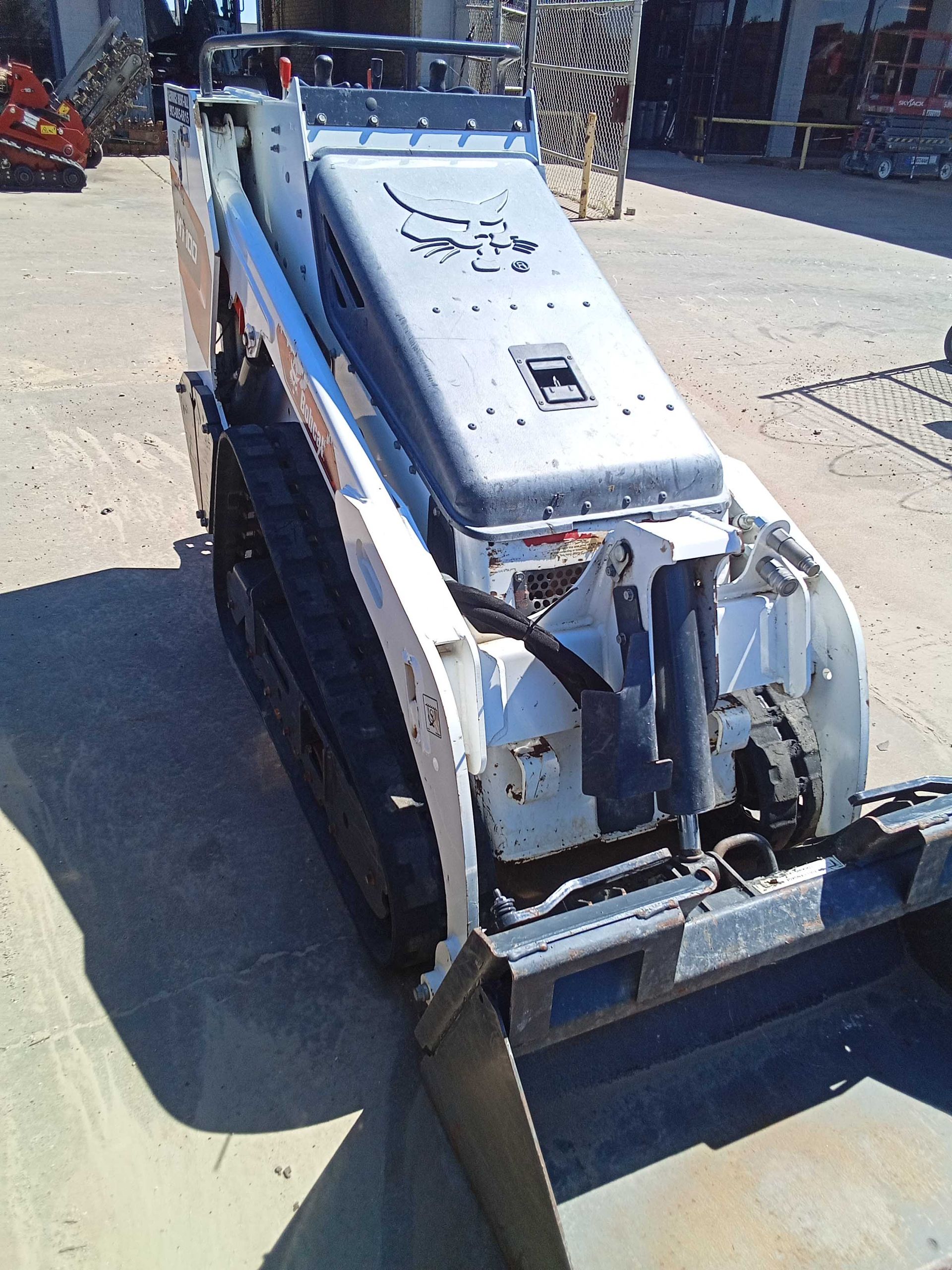 White and orange Bobcat tracked skid steer on a construction site, with a black bucket.