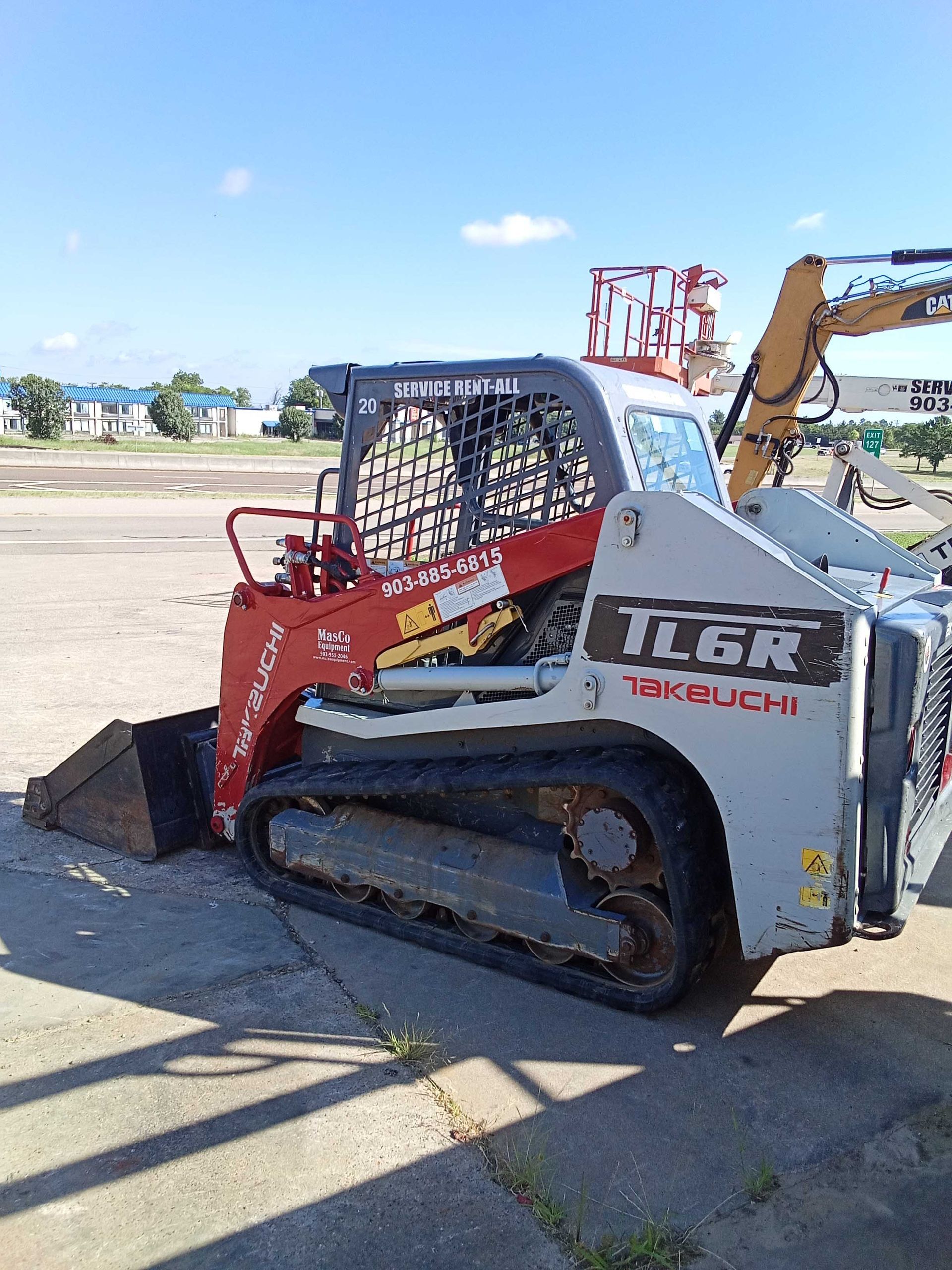 Gray and red Takeuchi TLGR track skid steer loader with bucket on a paved area.