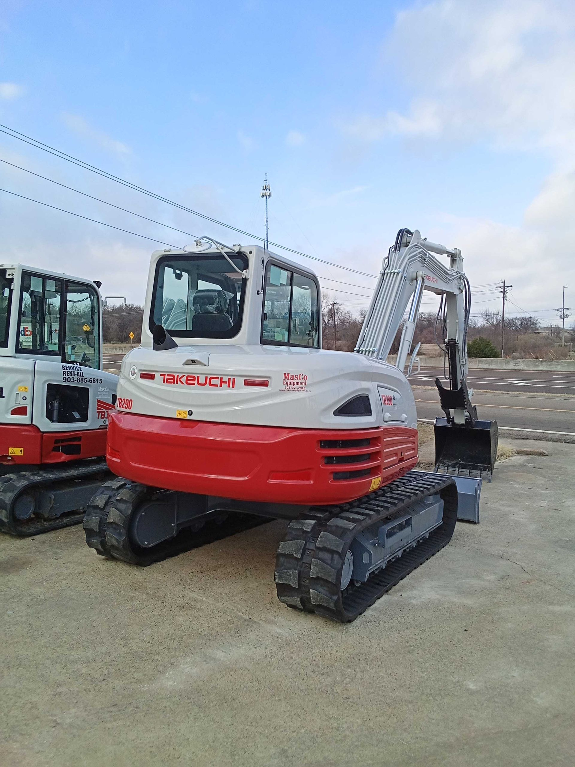 Red and white Takeuchi excavator on tracks. Outdoor setting with blue sky.