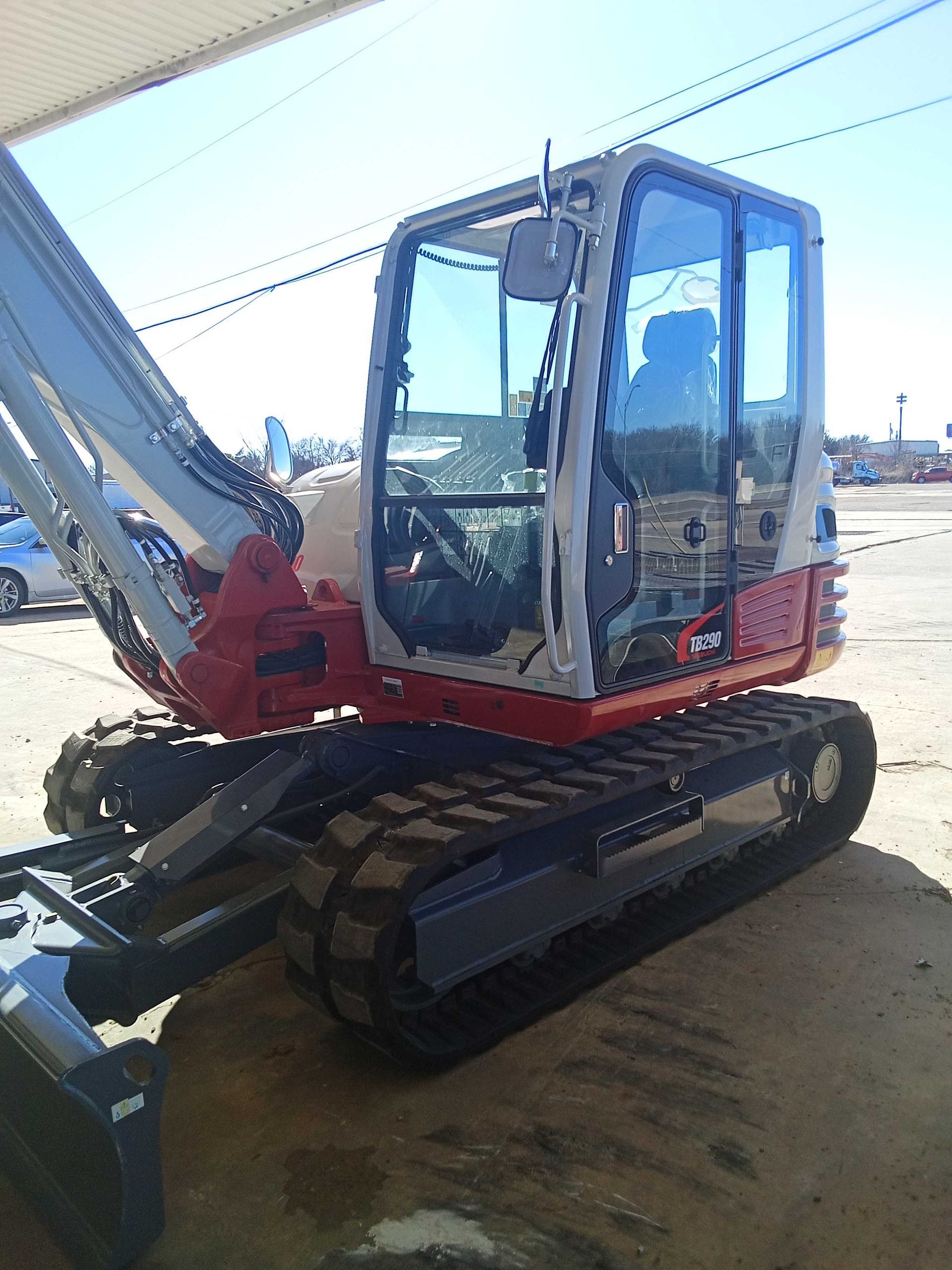 Red and white excavator on tracks, under a blue sky, outside.