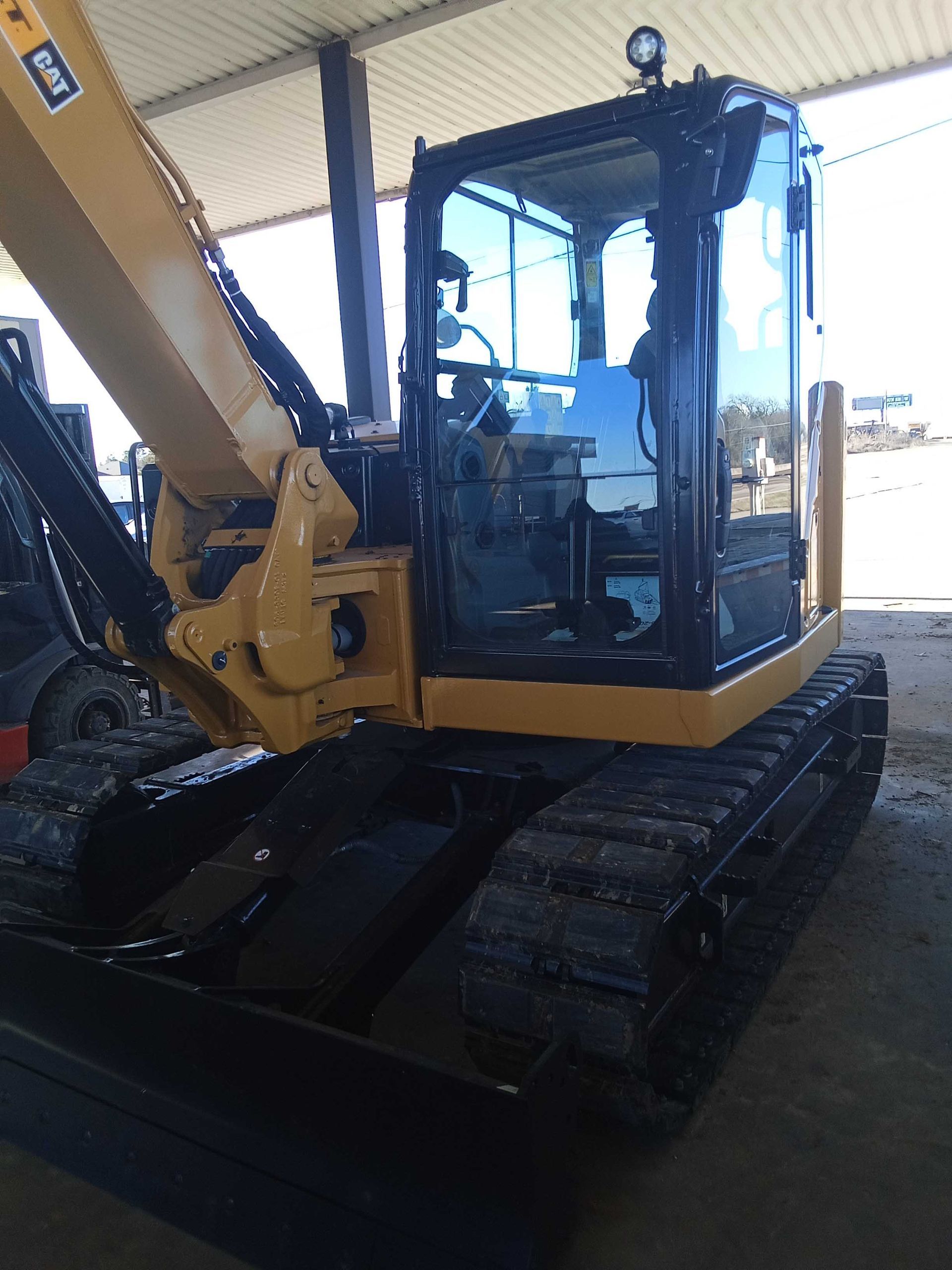 Yellow and black excavator in a warehouse, tracks visible, cab with windows.