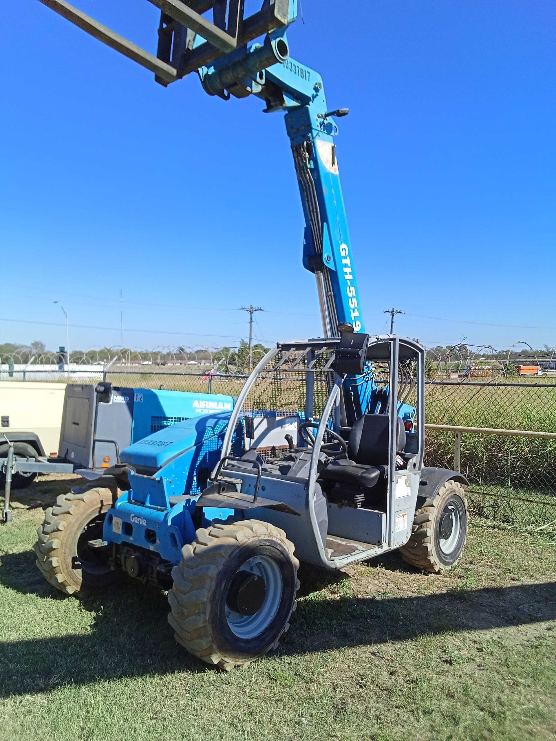 Blue Genie telehandler on grass, extending its boom against a blue sky.