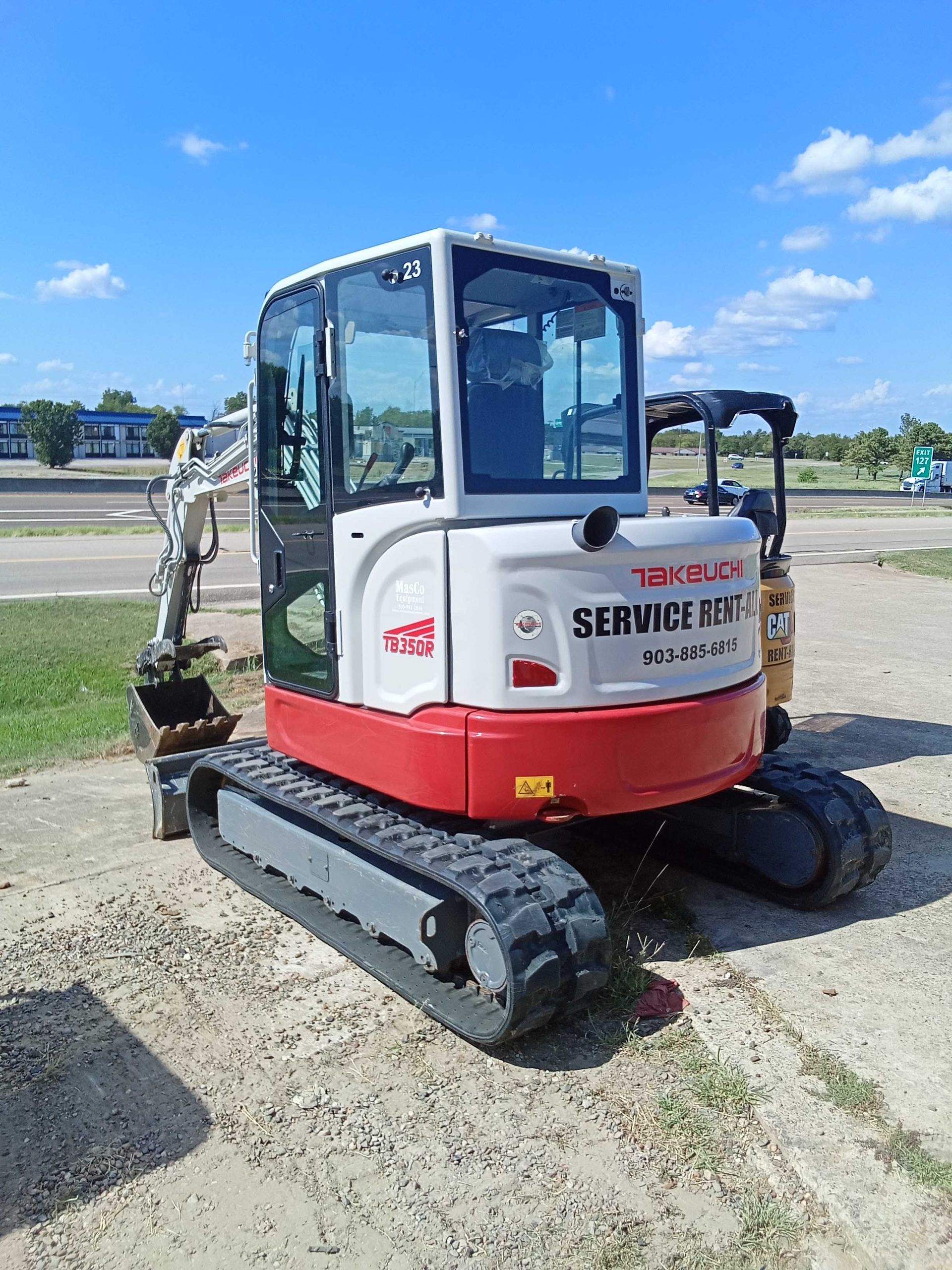 A red and white mini excavator on gravel, under a blue sky. 