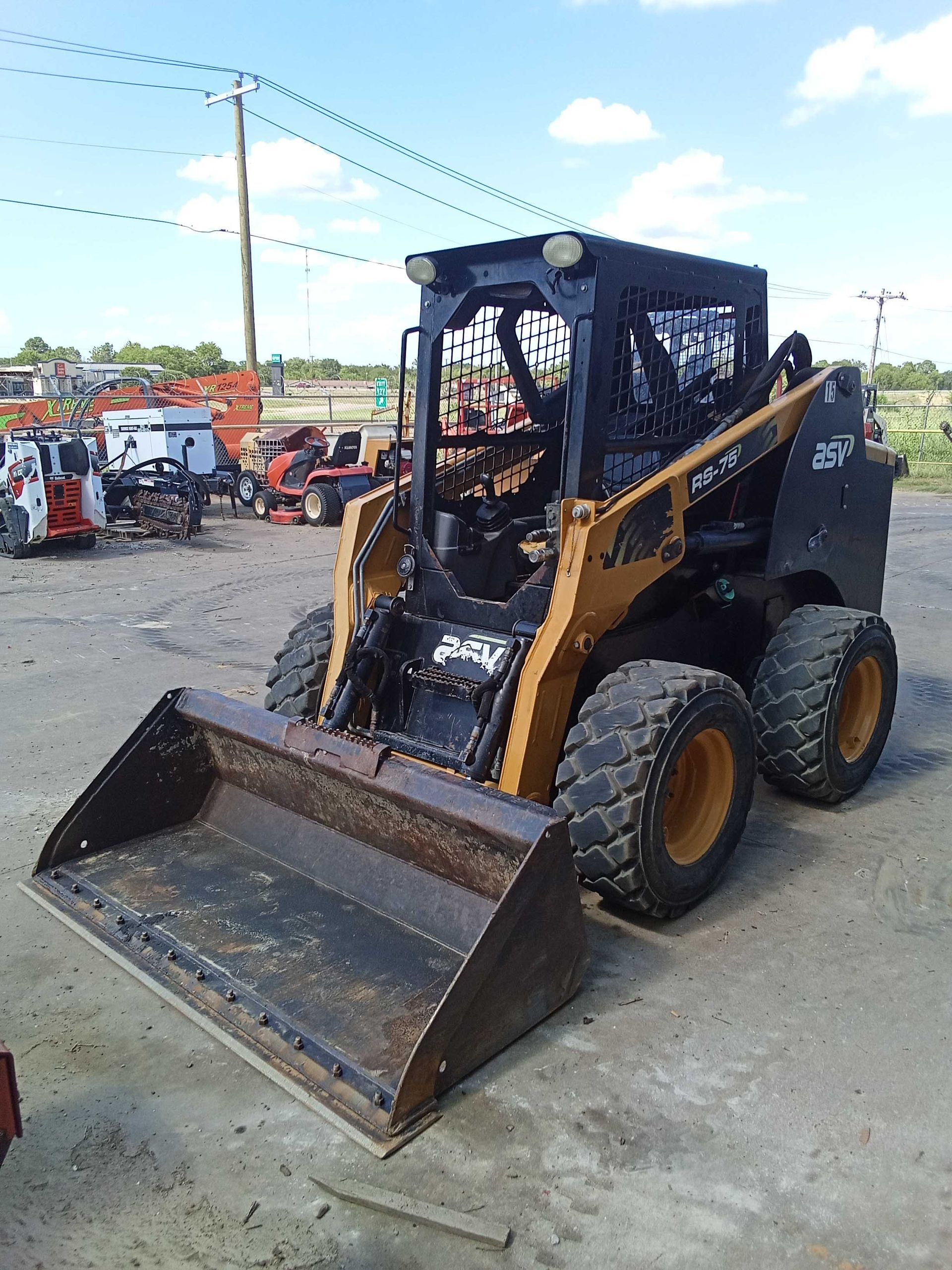 Brown and black skid steer loader with bucket outdoors on a sunny day.