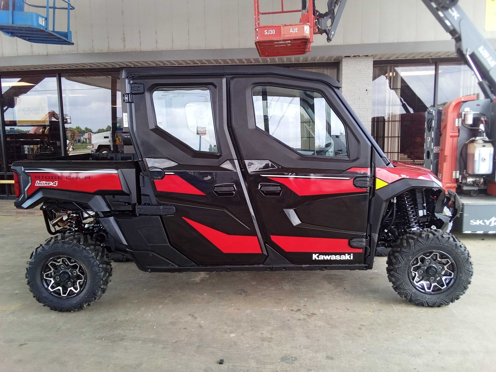Black and red Kawasaki UTV with black wheels and a cab, parked outside.