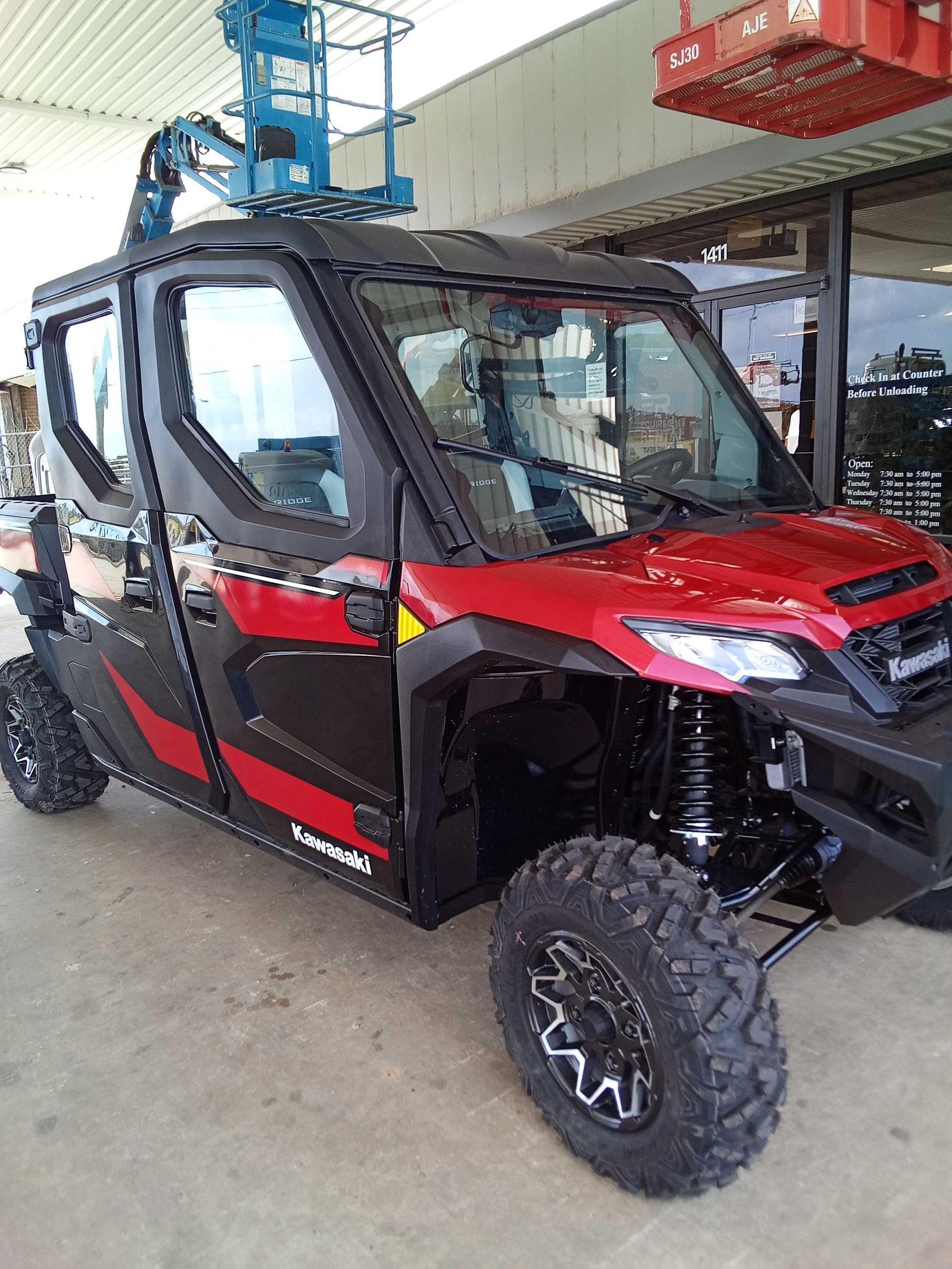 Red and black Kawasaki UTV with black wheels parked near a building with a lift above it.
