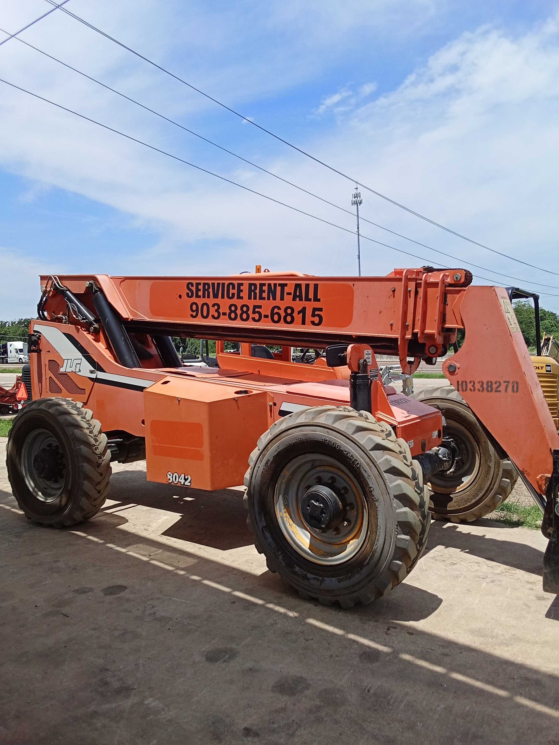 Orange construction telehandler with large tires, parked outdoors under a blue sky.