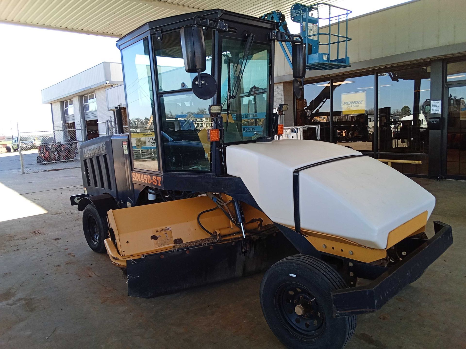 Yellow and black street sweeper with a white water tank, parked outdoors.